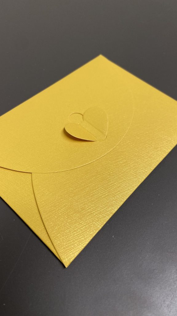 A yellow envelope with a heart-shaped butterfly fastening on a dark grey background. Representing the high-quality yellow envelopes that all Letters from poppy arrive in.